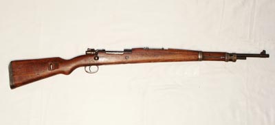 Zdjęcie karabinka Mauser M1948 o kalibrze 7,92 mm. Pochodzi z lat pięćdziesiątych XX w z Jugosławii. Broń w większości wykonana została z drewna koloru brązowego. Na górze tej drewnianej konstrukcji osadzone zostały metalowa lufa, zamek i przyrządy celownicze.